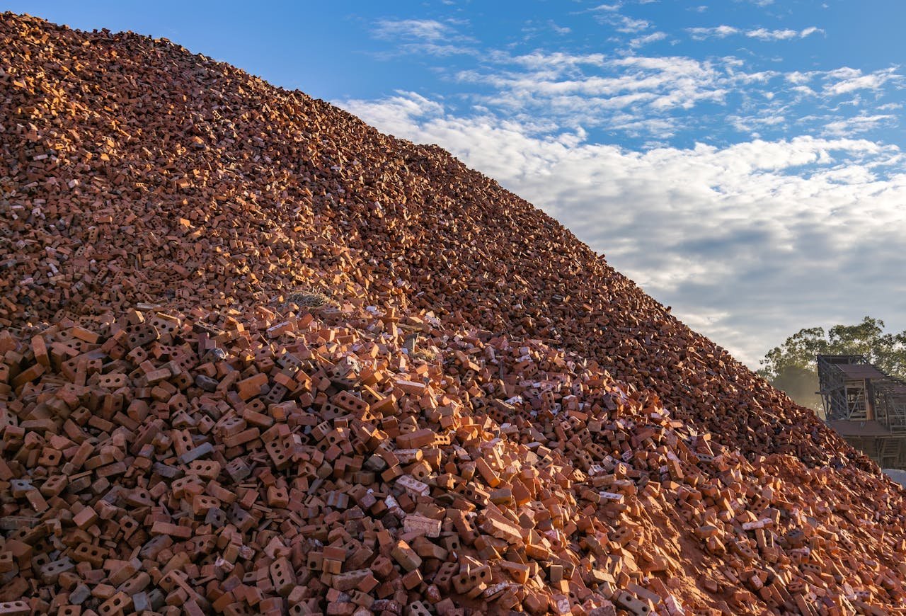 creative-02 Vast mound of red bricks stacked outdoors against blue skies and clouds.